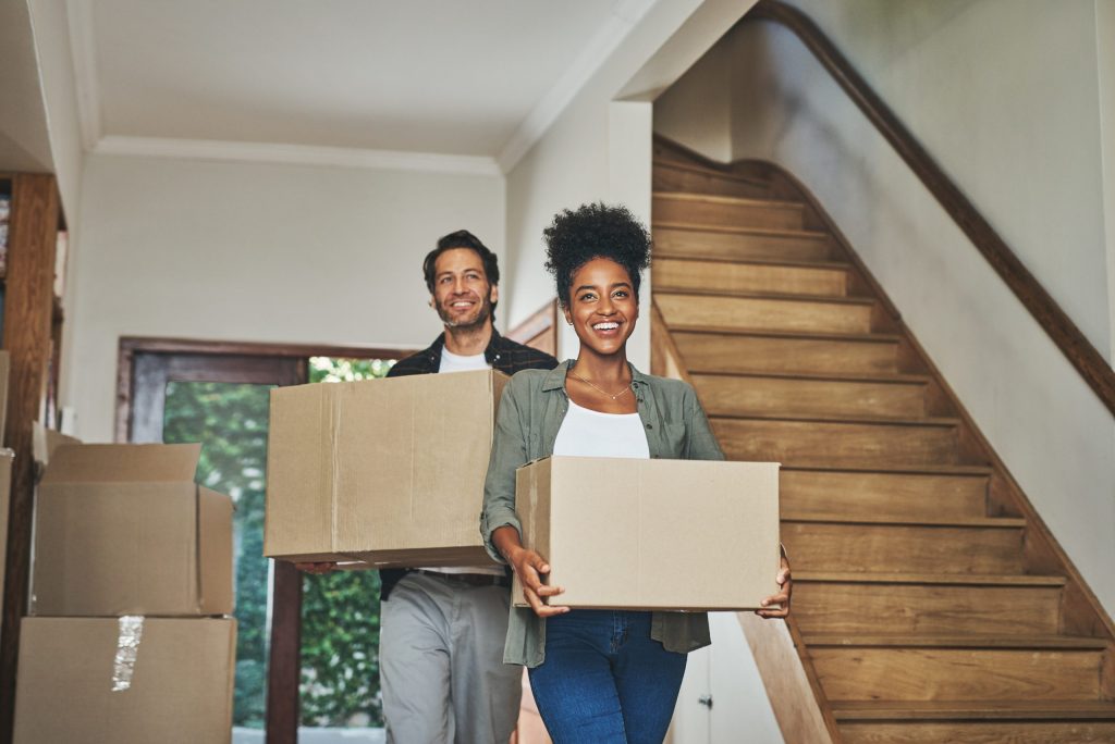 Man and woman walking inside a house with boxes; young couple moving into a house.